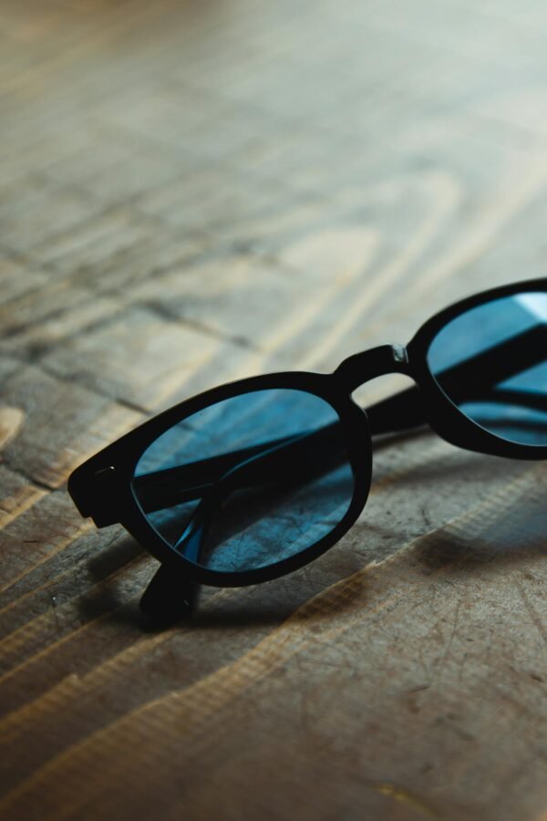 High angle trendy sunglasses with blue glass and black frames placed on wooden table