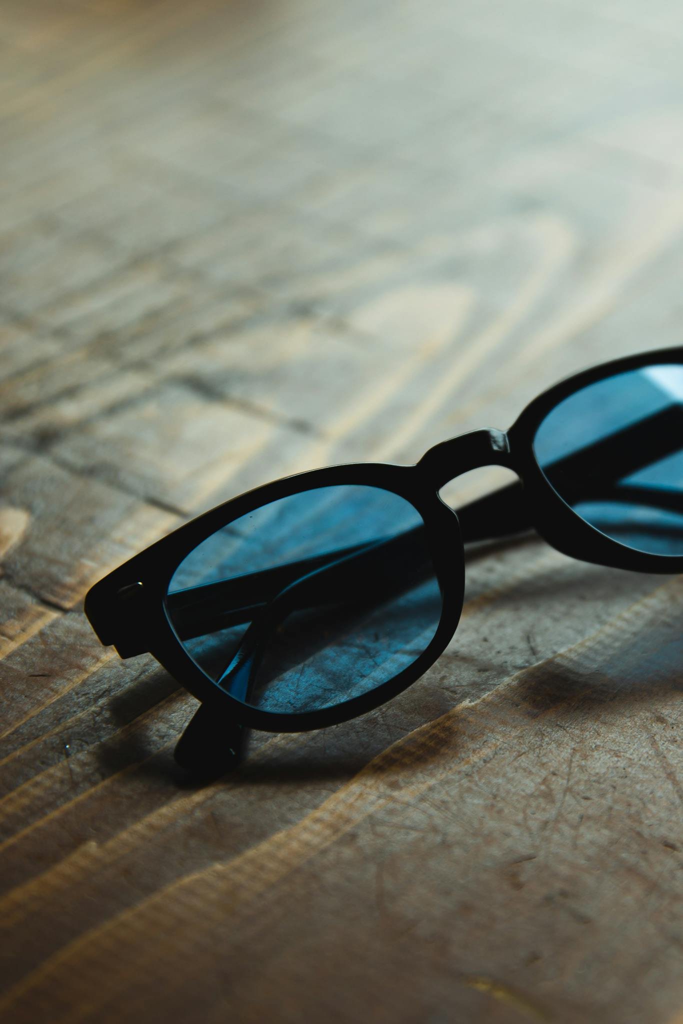 High angle trendy sunglasses with blue glass and black frames placed on wooden table