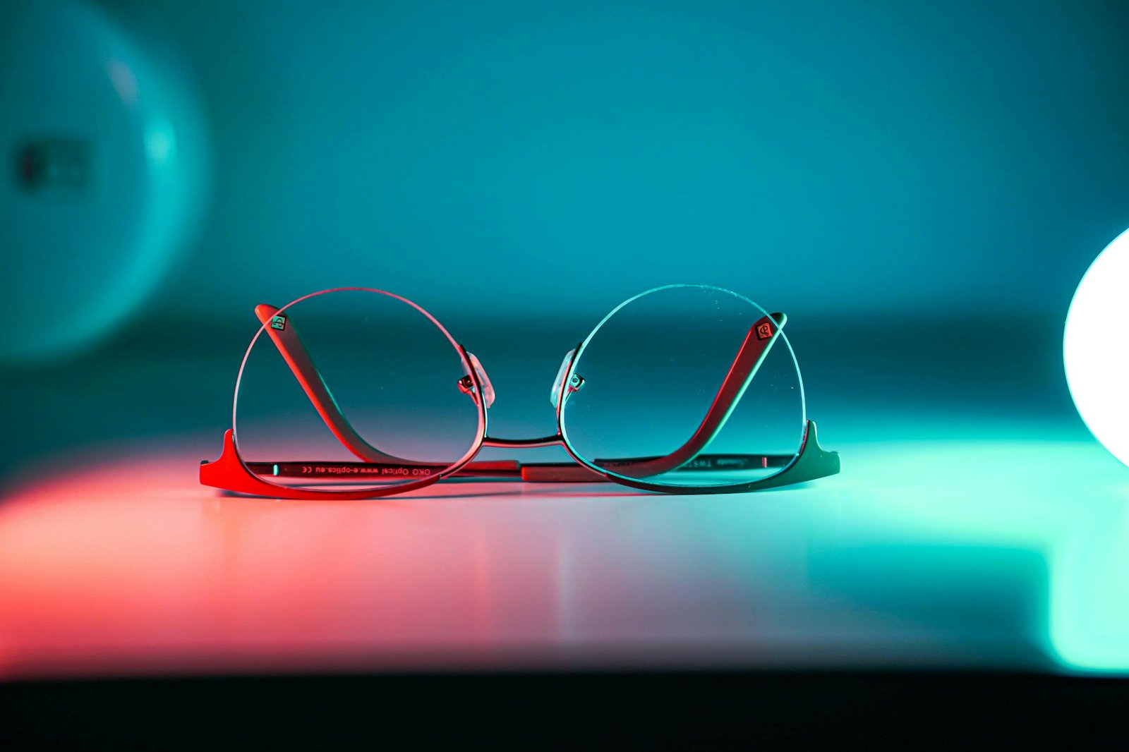 Stylish eyeglasses on a reflective surface with ambient neon lighting.