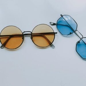 Two pairs of trendy sunglasses with geometric designs, one with orange lenses and the other with blue, on a white surface.