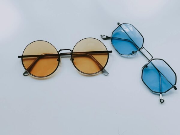 Two pairs of trendy sunglasses with geometric designs, one with orange lenses and the other with blue, on a white surface.