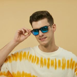 Young man wearing blue sunglasses and a tie-dye shirt poses against a yellow background.